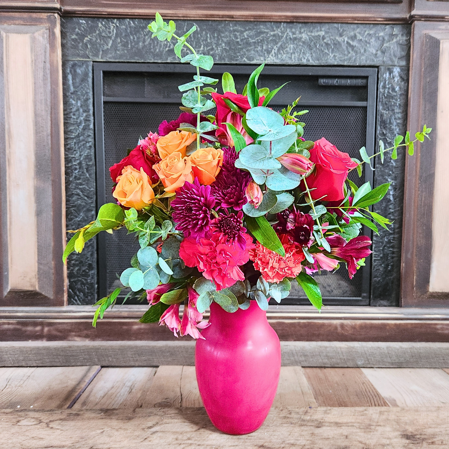 Colorful bouquet of flowers in a pink vase against a fireplace.