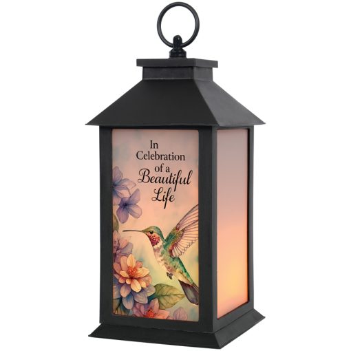 A frosted glass lantern with a black metal frame, featuring a floral and hummingbird design, and an inscription that reads 'In Celebration of a Beautiful Life'. It includes a flameless LED candle inside.