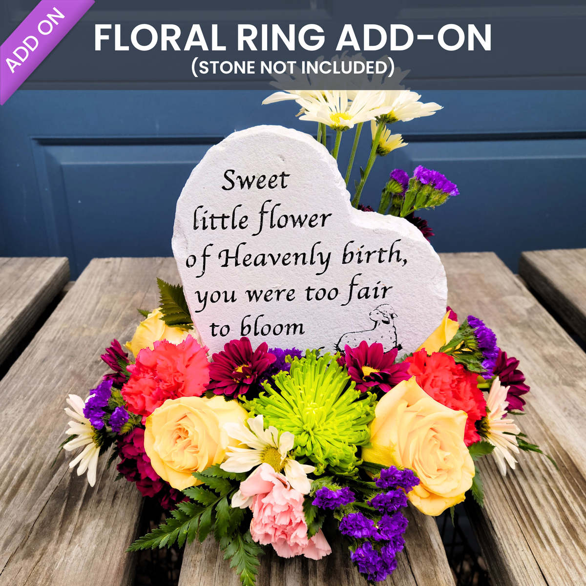 A floral memorial-style arrangement on a wooden table featuring a white heart-shaped stone plaque with printed text, surrounded by mixed flowers including yellow, pink, red, purple, green, and white blooms. Large overlaid text at the top reads 'FLORAL RING ADD-ON (STONE NOT INCLUDED)' with a purple 'ADD ON' banner.