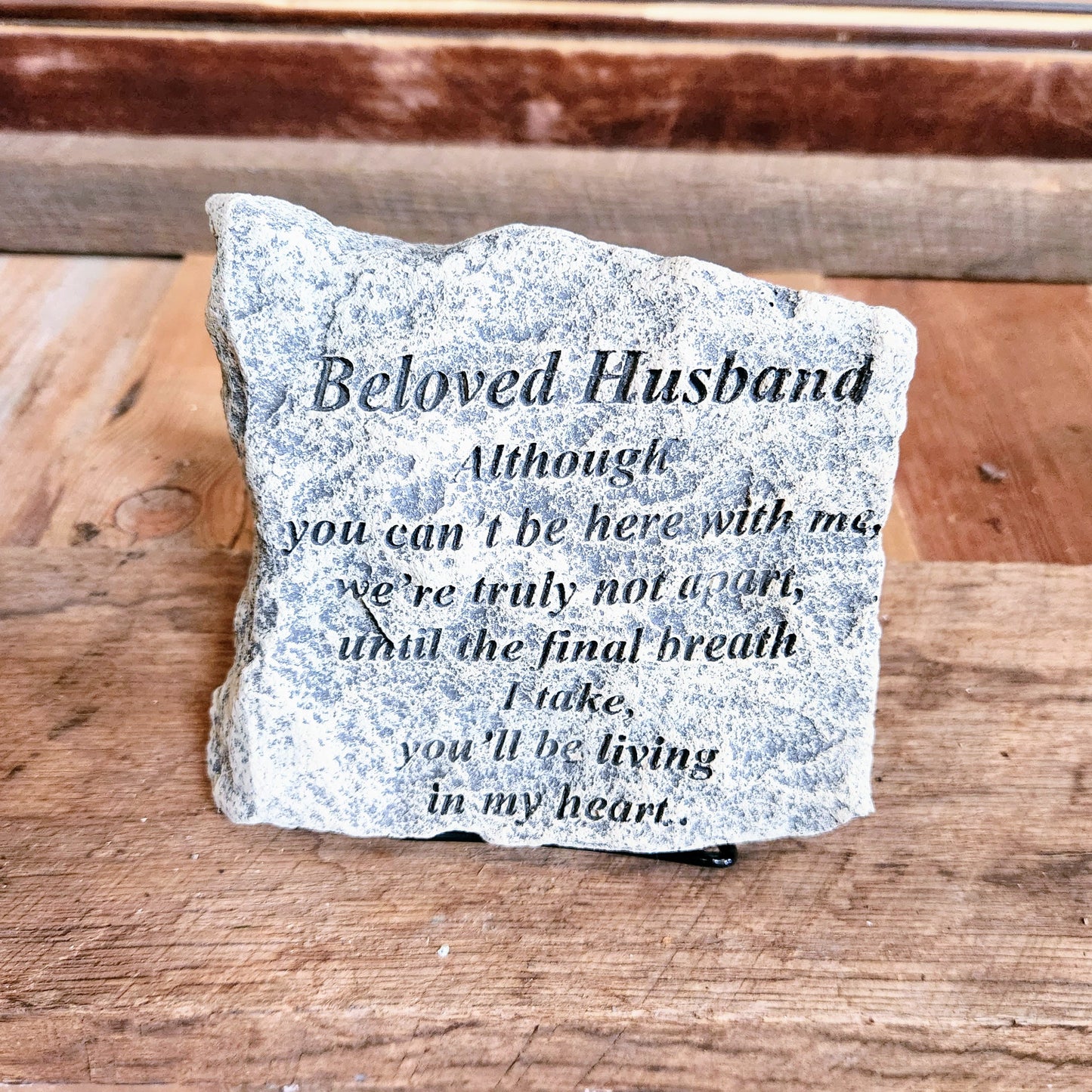 A gray concrete memorial plaque with the text 'Beloved Husband' carved on it, placed on a wooden surface.