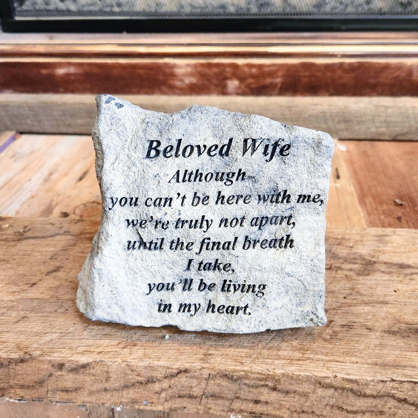 A small memorial stone with an inscribed message for a beloved wife, placed on a wooden surface.
