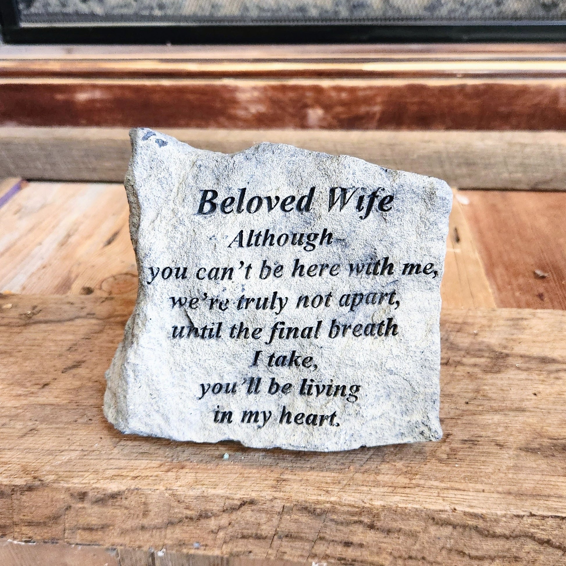 A small memorial stone with an inscribed message for a beloved wife, placed on a wooden surface.
