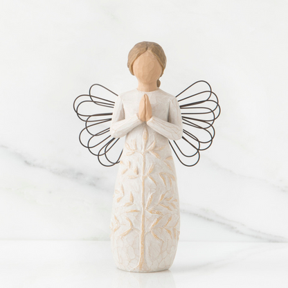 A figurine of a graceful angel with hands folded in prayer, dressed in a dress with a tree pattern, made of willow wood, placed on a marble surface.