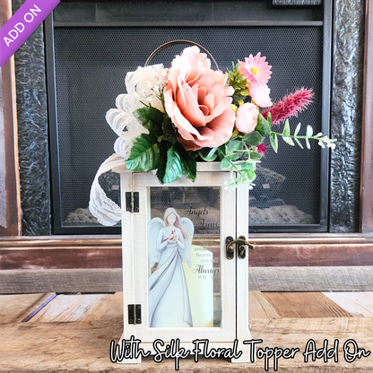 Decorative lantern with angel figure and floral topper on a wooden surface.