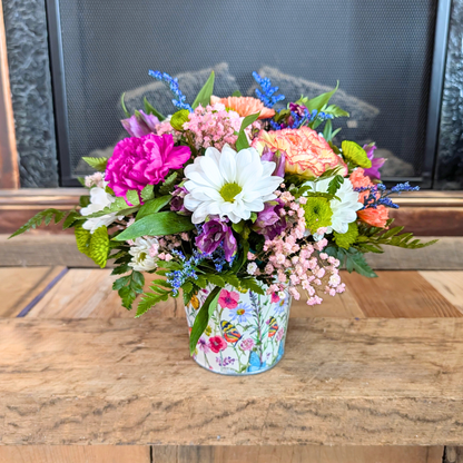 Colorful flower arrangement in a floral-patterned pot on a wooden surface.