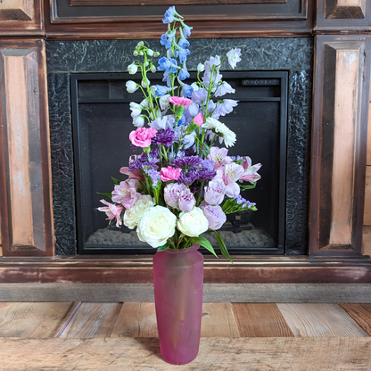 Cotton Candy Skies Bouquet with soft blue, lavender, pink, purple and white flowers arranged in a pink glass vase at Treasured Roots Flower Shop in Hoopeston, IL.