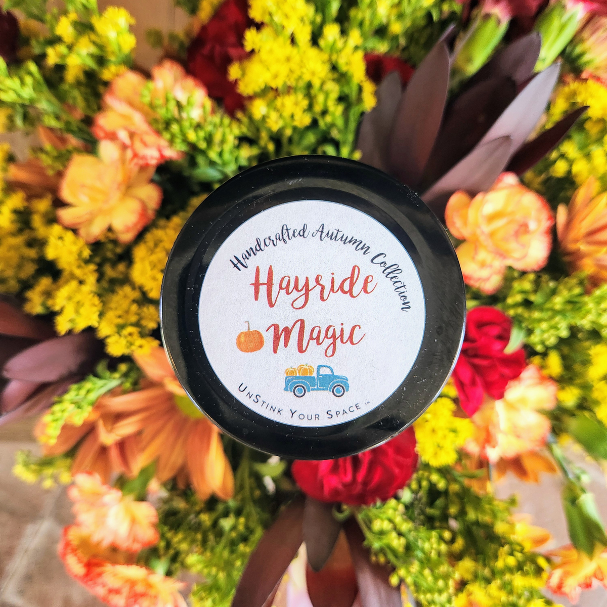 Close-up of Cozy Glow Centerpiece showing fall flowers, solidago, mixed greenery, and a mason jar soy candle from Treasured Roots Flower Shop in Hoopeston, IL.