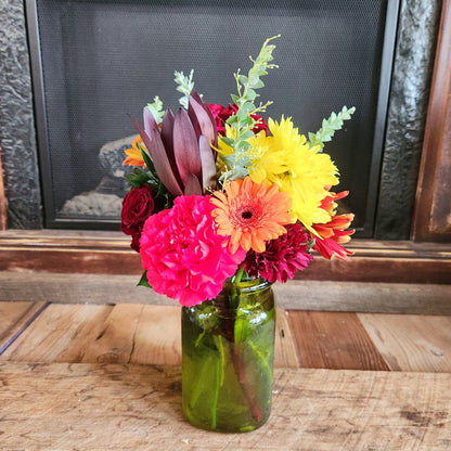 Crimson Crush fall bouquet with rich red and burgundy flowers, bright orange, yellow and pink blooms, eucalyptus, and greenery in a green fall jar vase from Treasured Roots Flower Shop in Hoopeston, IL.