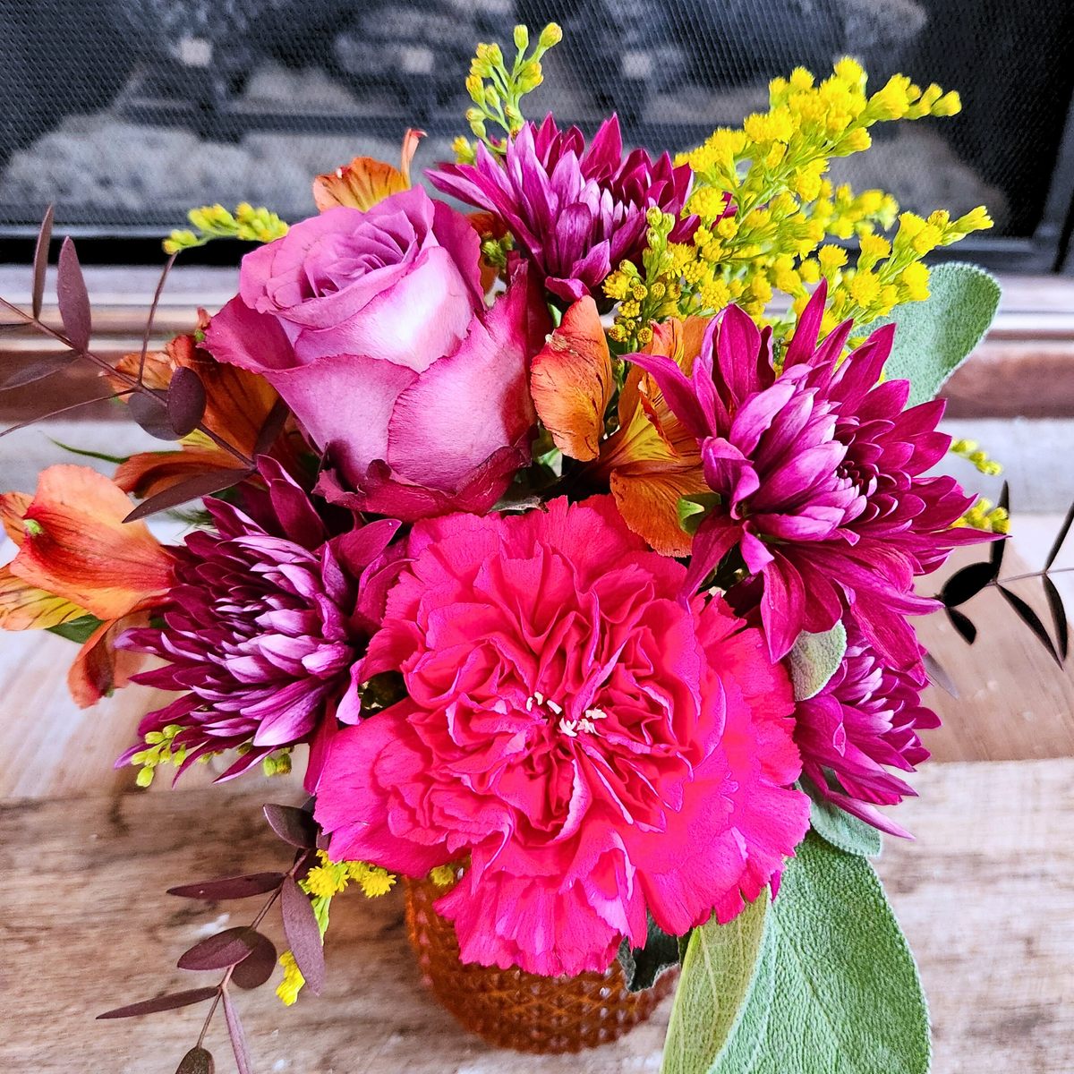 Close-up of Harvest Sunset showing pink, purple, orange, and yellow fall flowers with mixed fresh greenery from Treasured Roots Flower Shop in Hoopeston, IL.