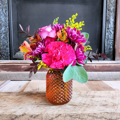 Harvest Sunset petite fall flower arrangement with pink, purple, orange, and yellow blooms in a textured red or orange jar vase from Treasured Roots Flower Shop in Hoopeston, IL.