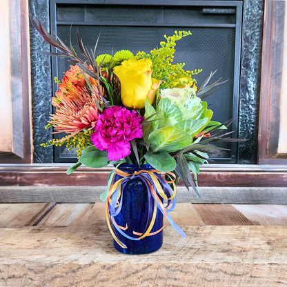 Kale Yeah, It’s Fall bouquet with ornamental kale, roses, mums, seasonal flowers, and ribbon accents in a blue vase from Treasured Roots Flower Shop in Hoopeston, IL.