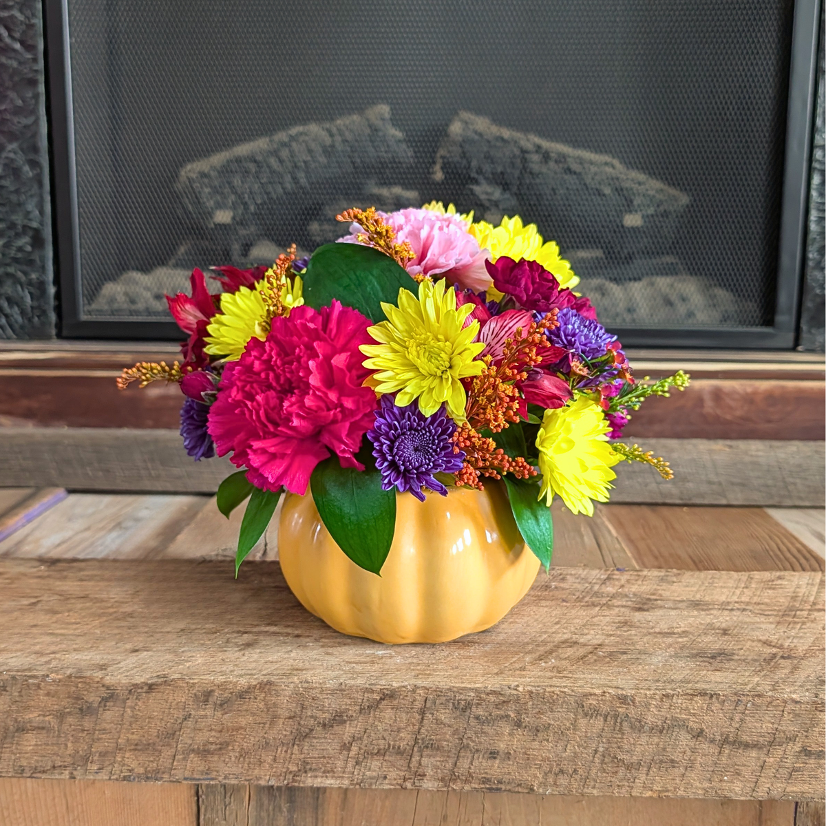 Close-up of Pick of the Patch showing colorful fall flowers including yellow, red, pink, burgundy, and purple blooms in a pumpkin container from Treasured Roots Flower Shop in Hoopeston, IL.