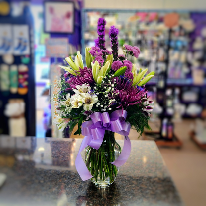 Tall purple and white vase bouquet with soft pink accents and mixed seasonal flowers in a glass container.