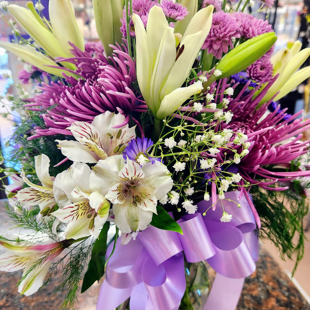 Tall purple and white vase bouquet with soft pink accents and mixed seasonal flowers in a glass container.