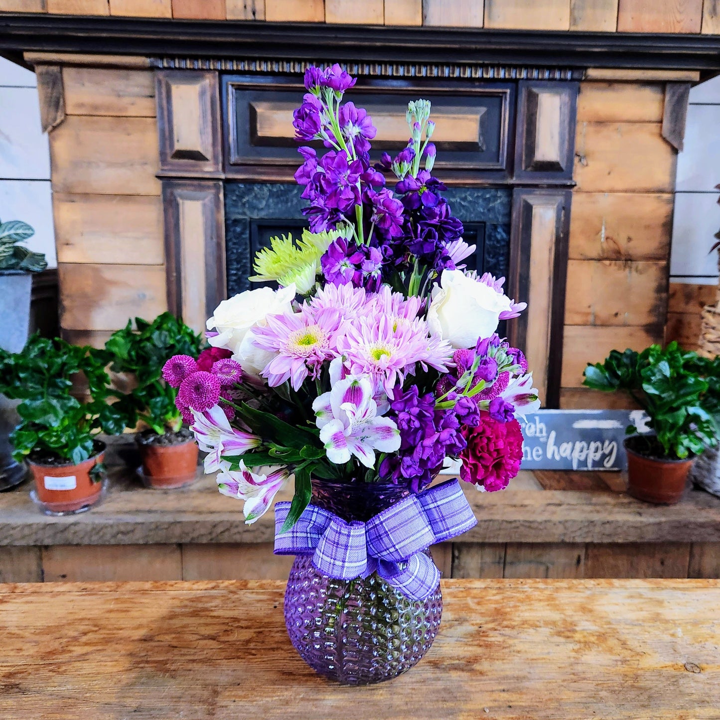 Tall purple and white vase bouquet with soft pink accents and mixed seasonal flowers in a glass container.